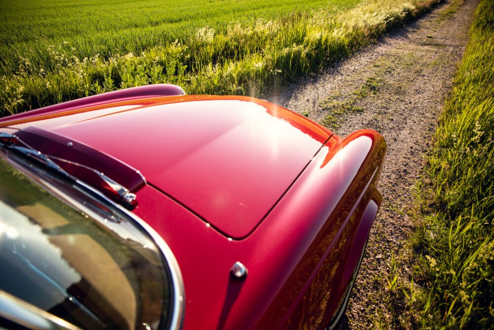 Red vintage car on rural path at sunset.