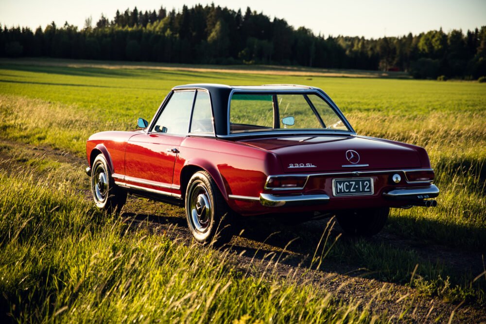 Vintage red Mercedes-Benz 230SL parked in countryside.