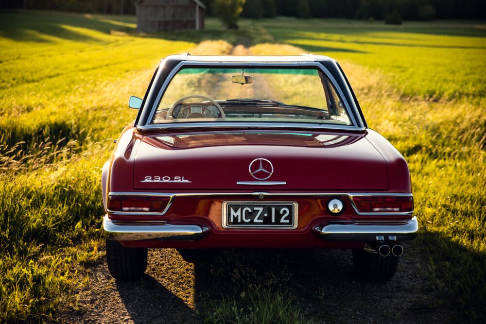 Red Mercedes 280SL on country road at sunset.