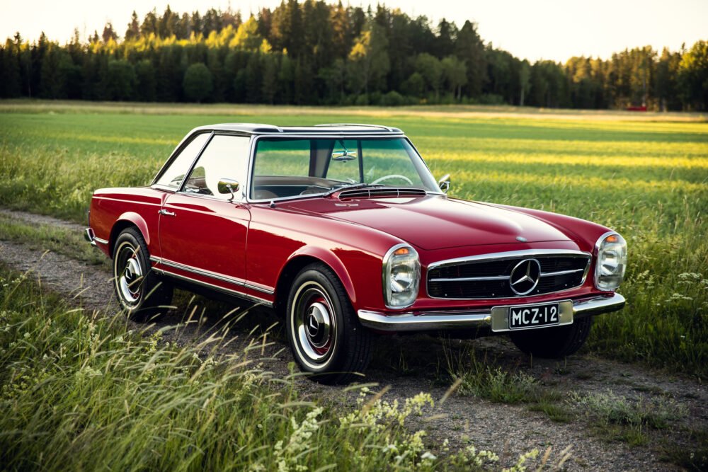 Vintage red Mercedes-Benz in lush green field.