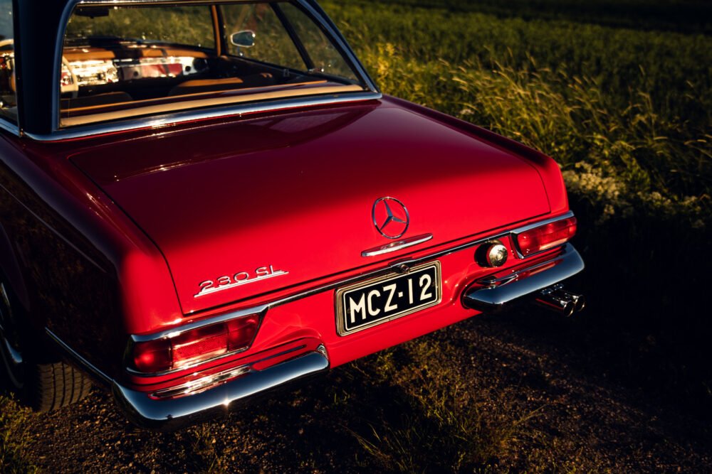 Red Mercedes 280 SL at sunset in grassy field.