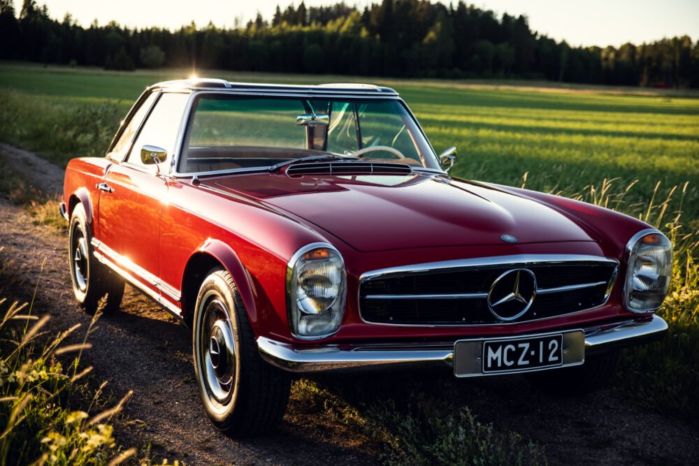 Vintage red Mercedes convertible parked in countryside at sunset.