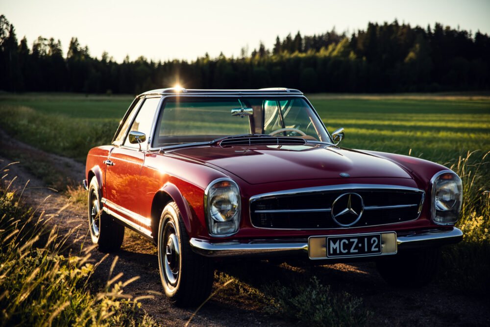 Vintage red Mercedes-Benz car in countryside at sunset.