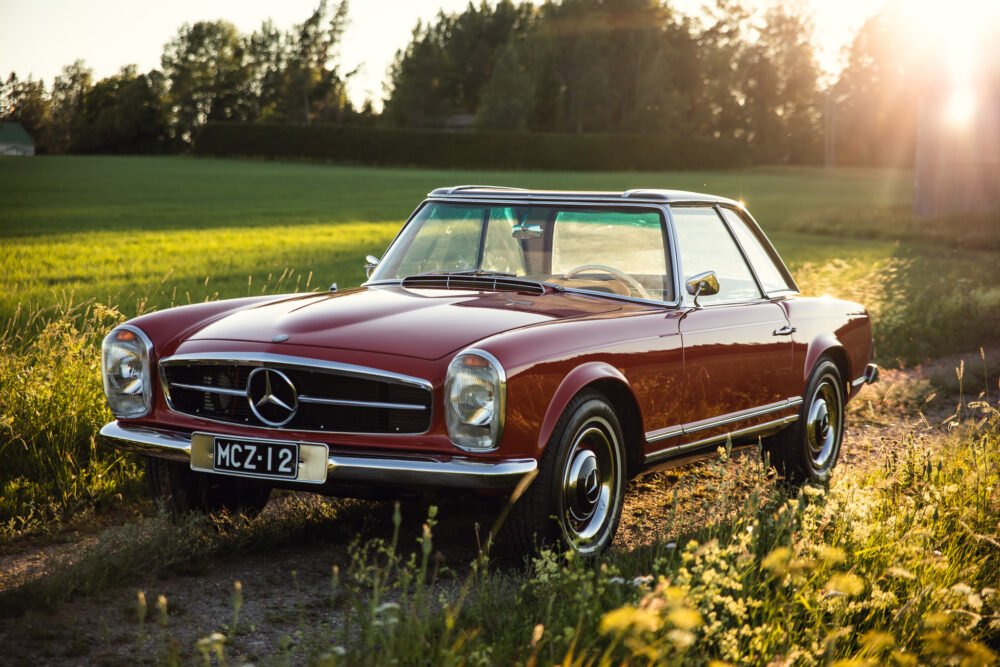 Vintage red Mercedes convertible in countryside at sunset.