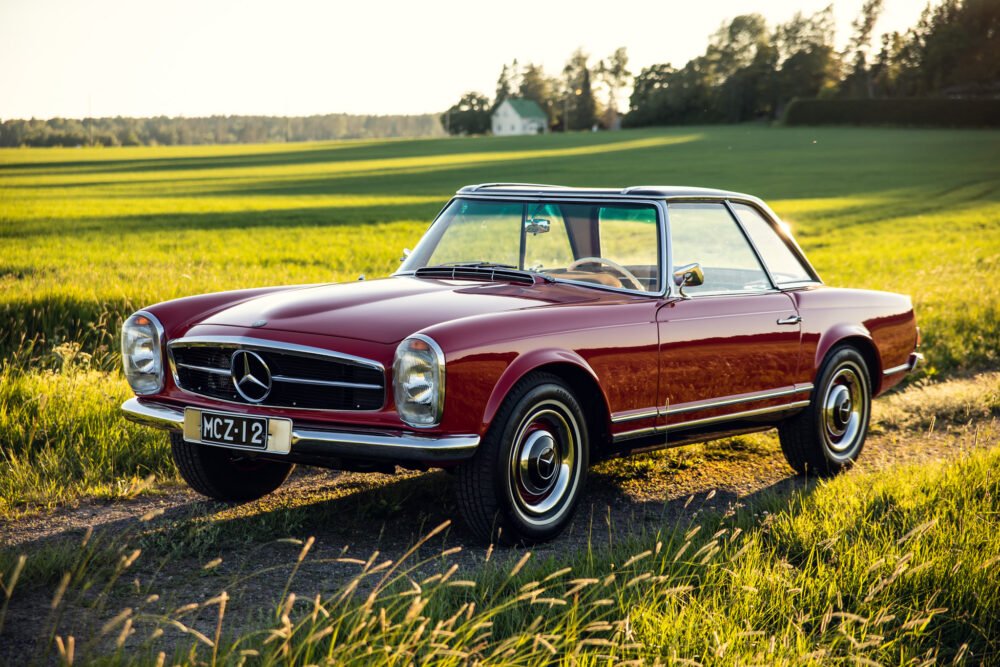 Vintage red Mercedes convertible in sunlit field.