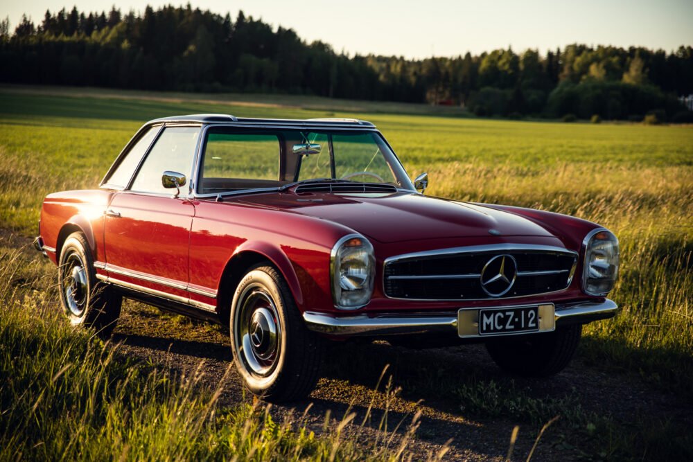 Red vintage Mercedes convertible in countryside at sunset.