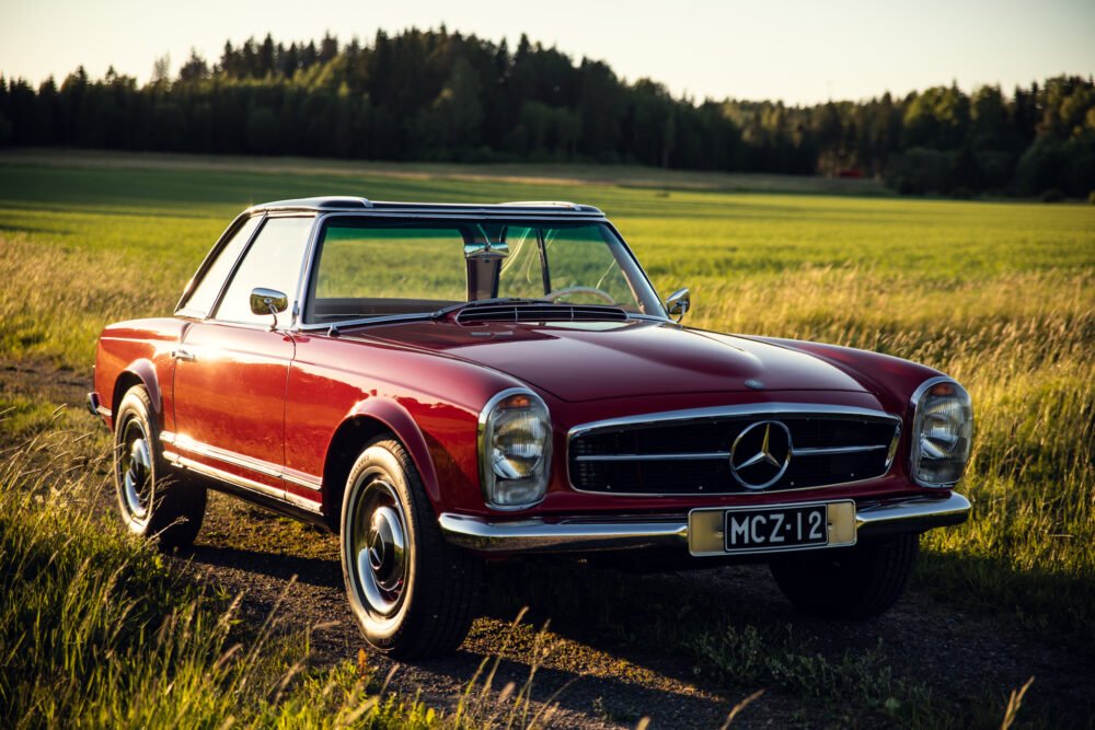 Classic red Mercedes convertible in sunlit field.