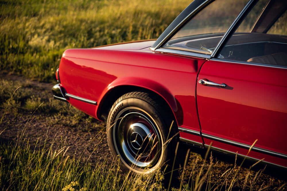 Red vintage car in golden hour grassland.