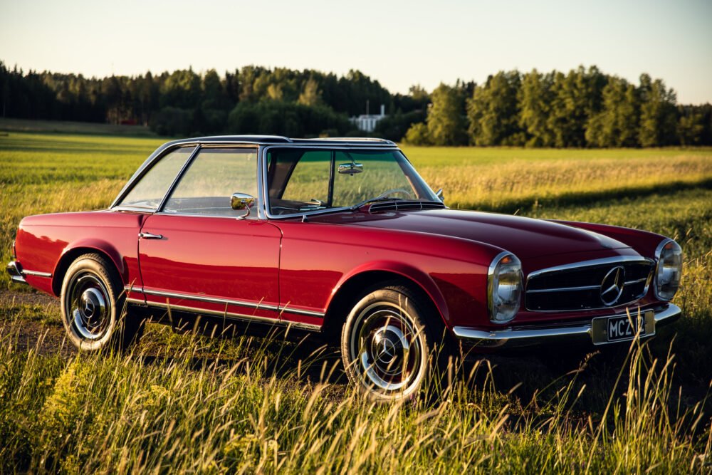 Vintage red Mercedes convertible in a field at sunset.