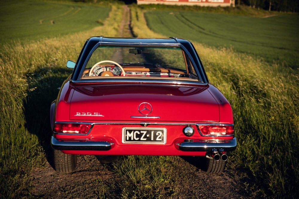 Red Mercedes 280SL on rural road at sunset.