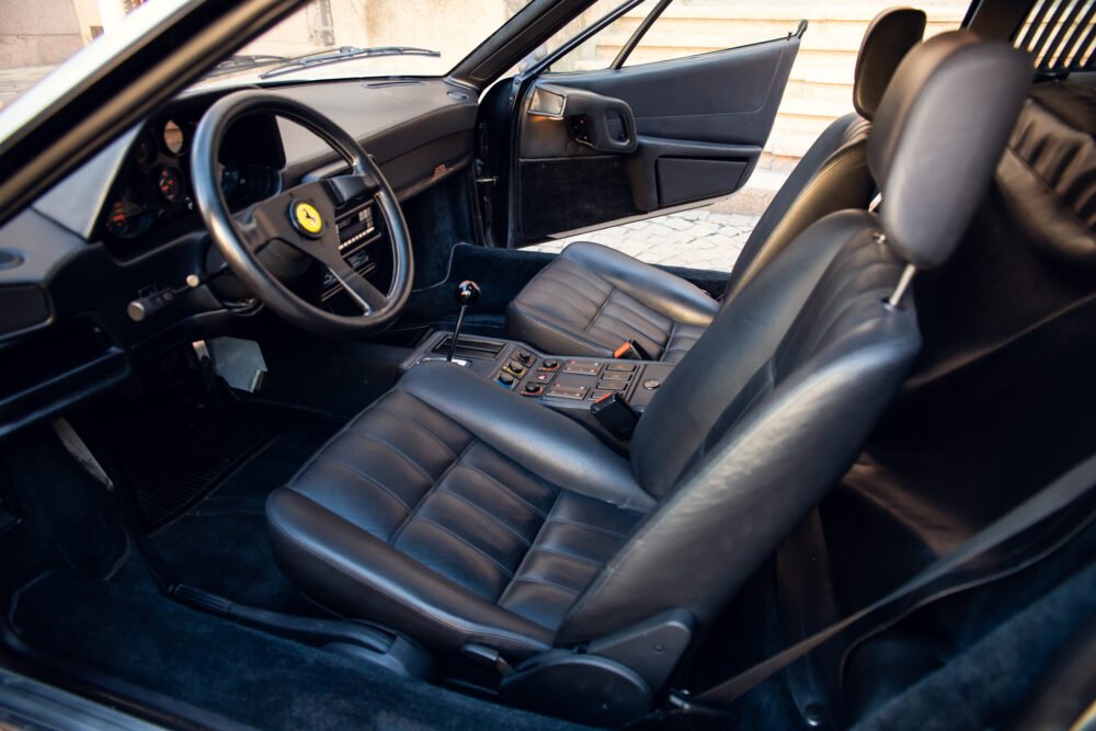 Vintage black Ferrari interior, leather seats, dashboard view.
