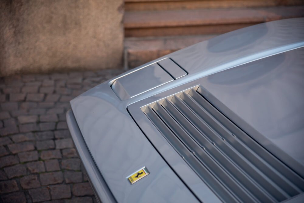 Close-up of silver car's hood with Ferrari logo.