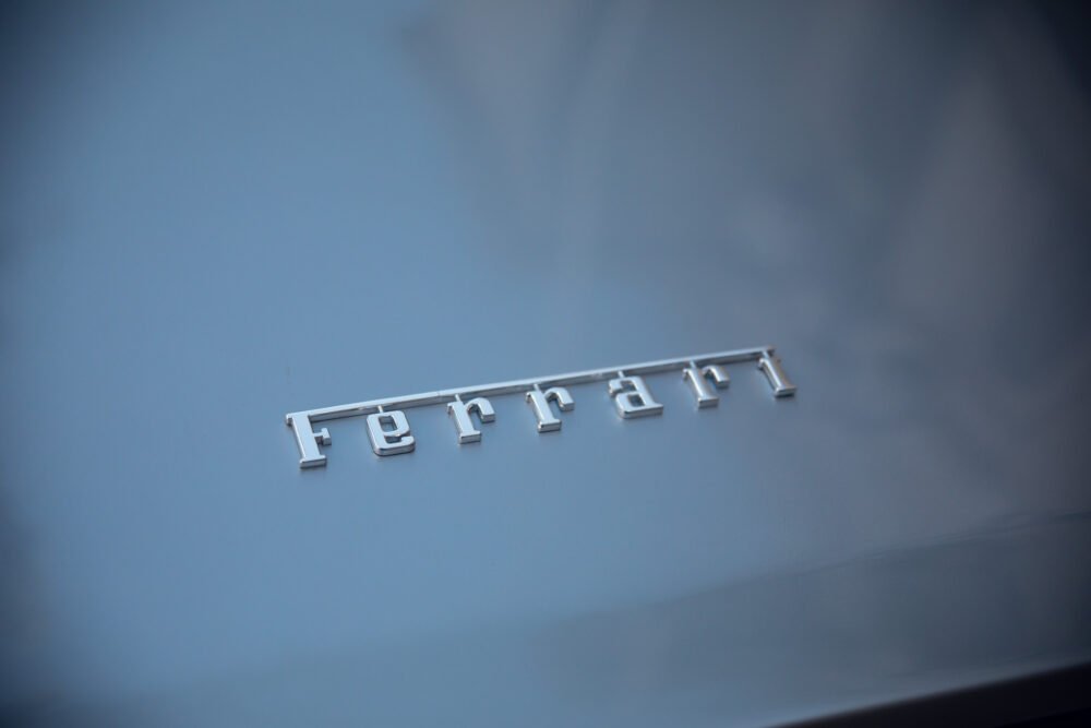 Close-up of silver Ferrari logo on blue car hood.