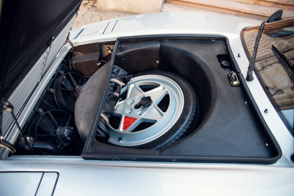 Spare wheel stored in open trunk of vintage car.