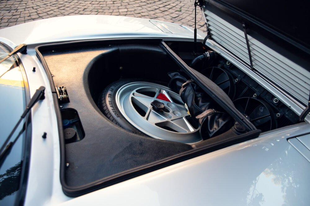 Spare tire stored in sports car's open trunk.
