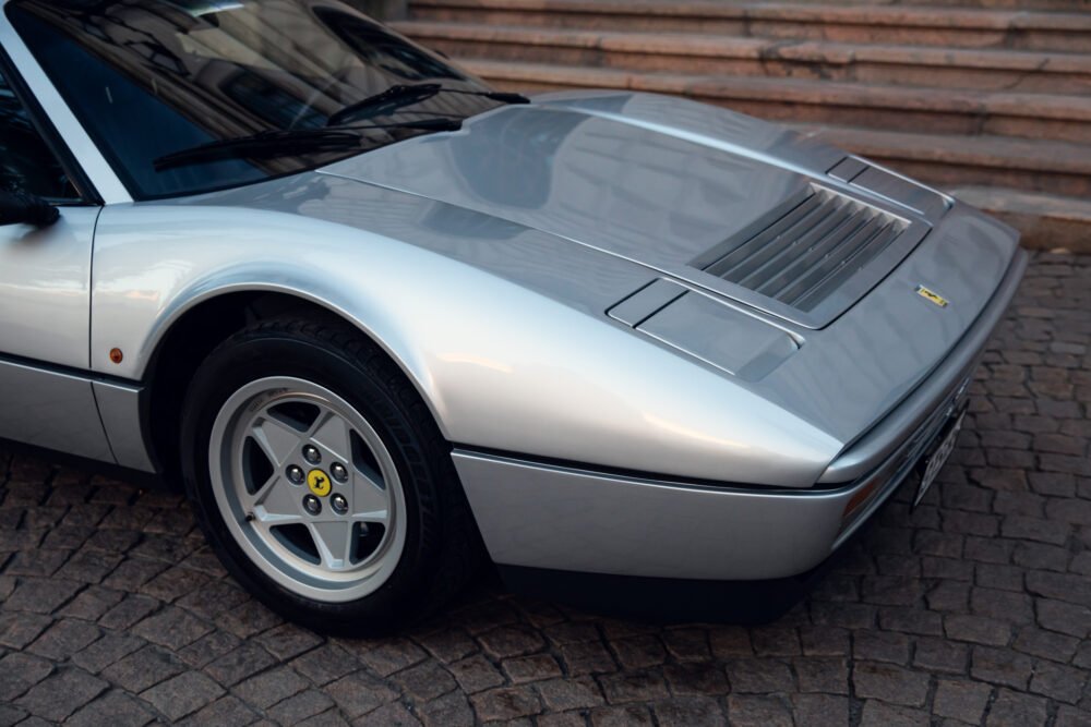 Silver Ferrari vintage sports car, cobblestone background.