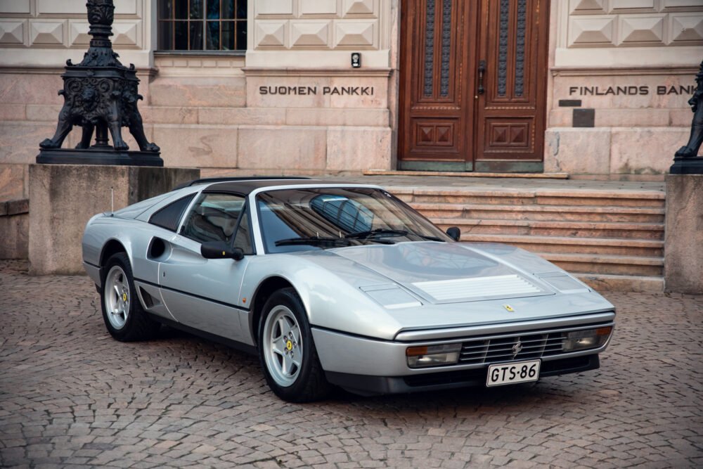 Silver Ferrari 328 parked in front of historic building.