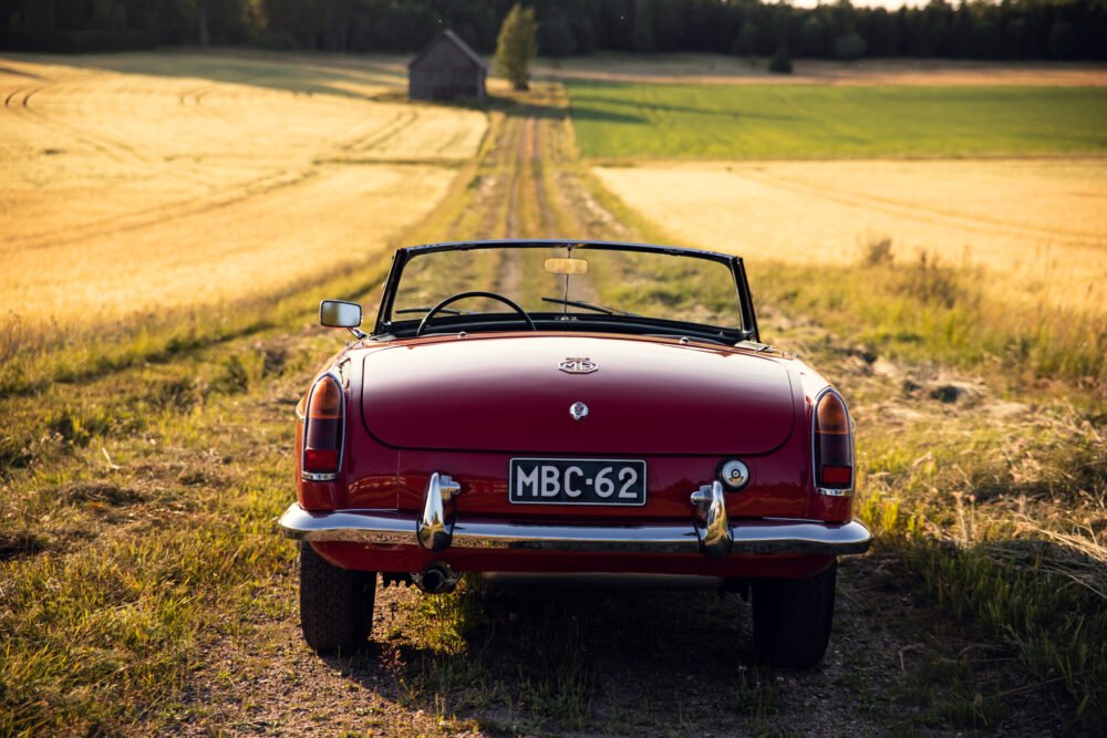 Vintage red convertible car on rural road at sunset.