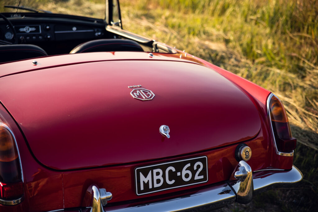 Red vintage MG car in grassy field.
