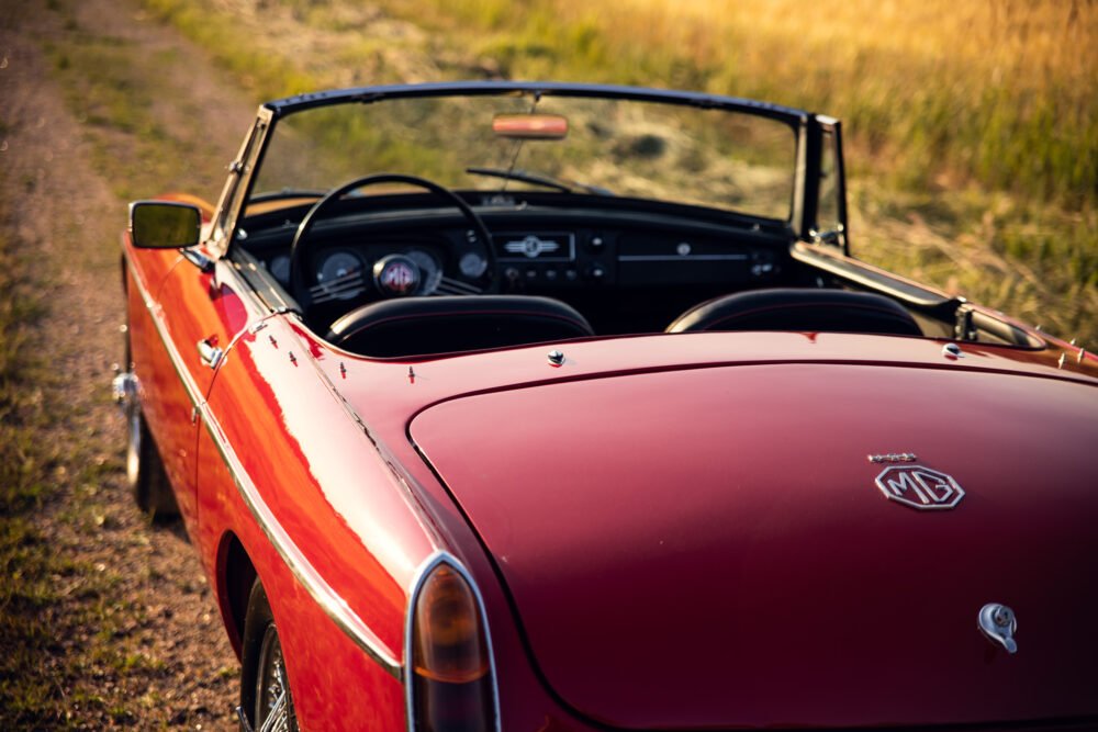 Vintage red MG convertible car on grassy path.