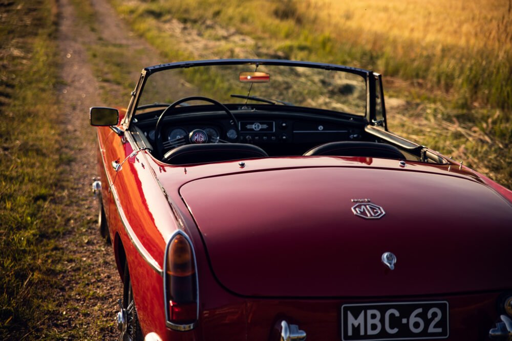 Red vintage MG convertible on country road at sunset.