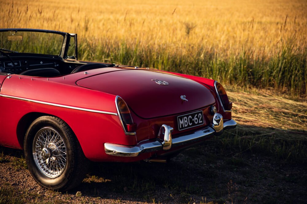 Red vintage convertible car in golden field at sunset.