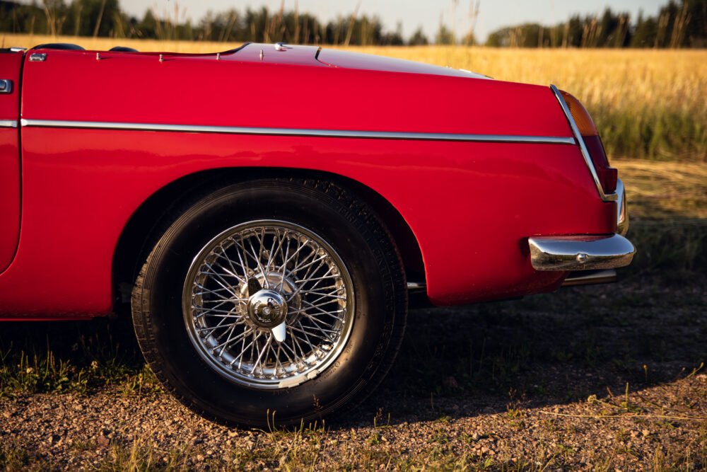 Red vintage car with chrome wheel parked by field.
