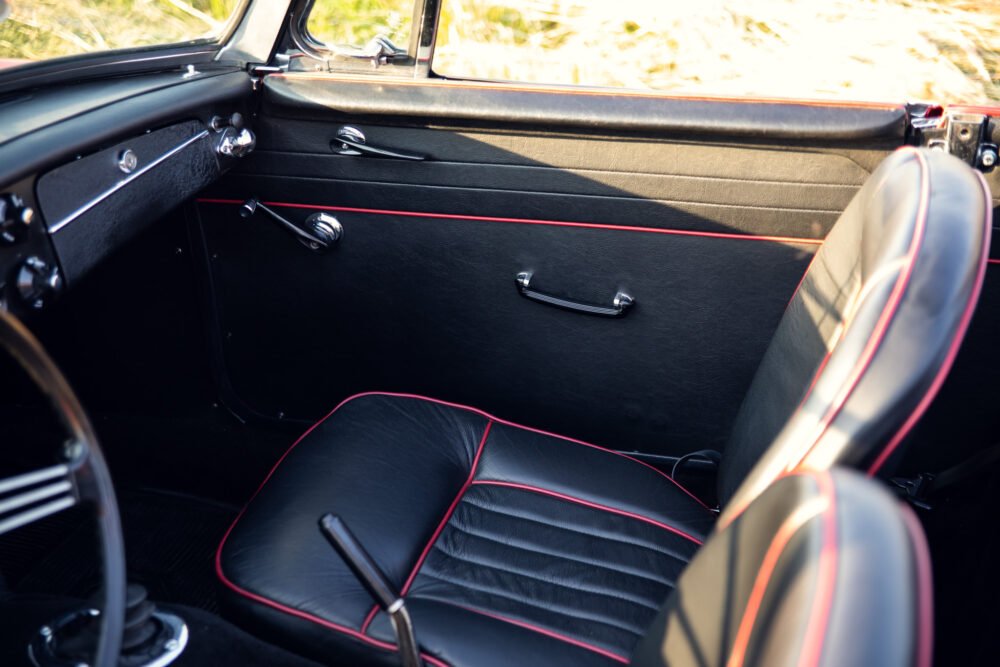 Vintage car interior with red-trimmed black leather seats.