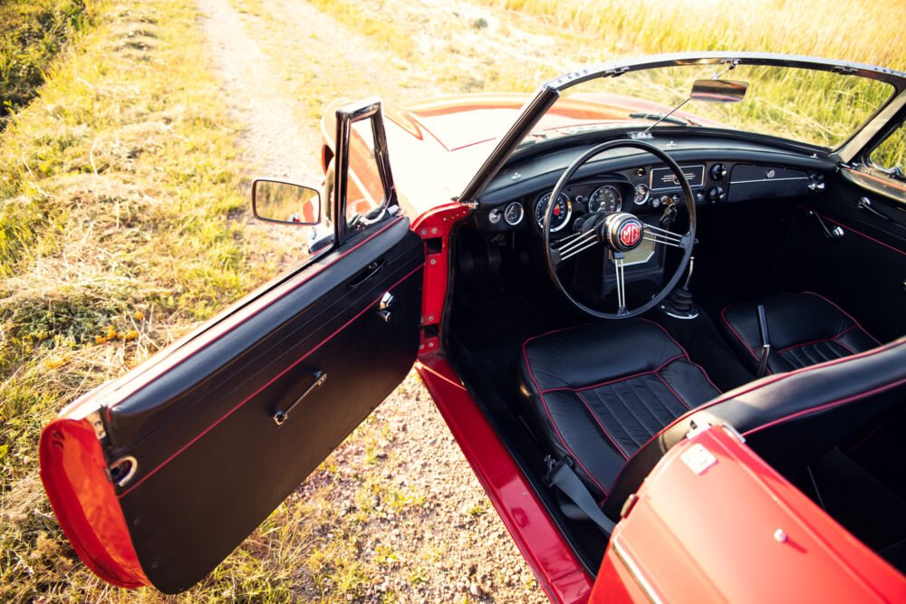 Red vintage convertible car with open door, countryside road.