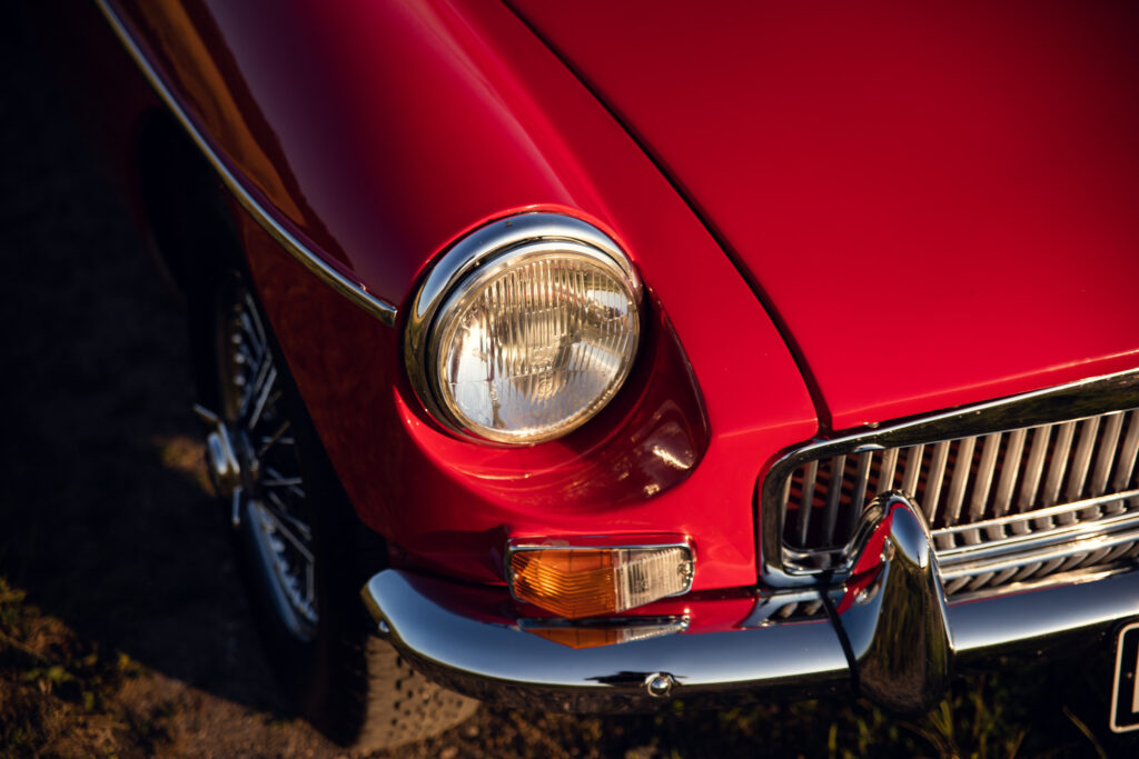 Close-up of vintage red car's front grille and headlight.