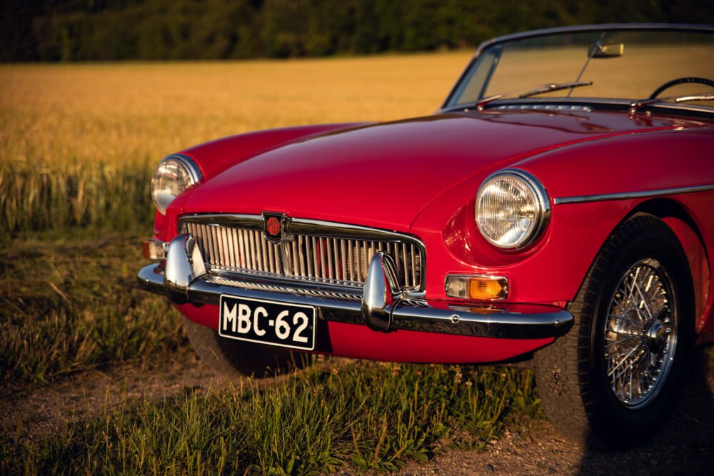Red vintage MG car in golden field at sunset.