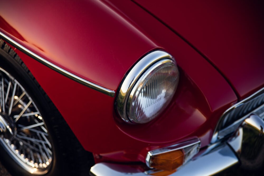 Close-up of red vintage car's headlight and chrome details.