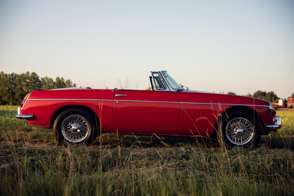 Red vintage convertible car in sunlit field.