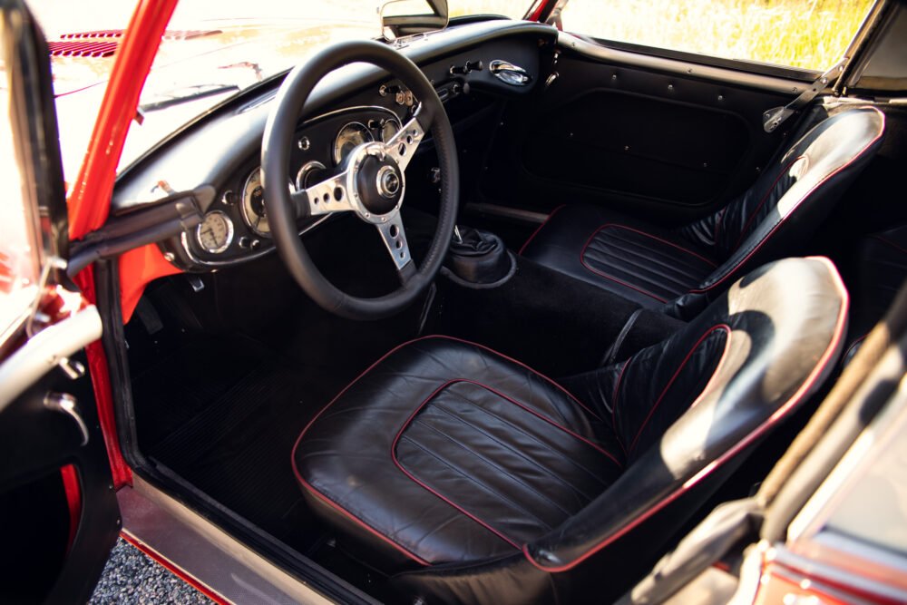 Vintage car interior with red accents and steering wheel.