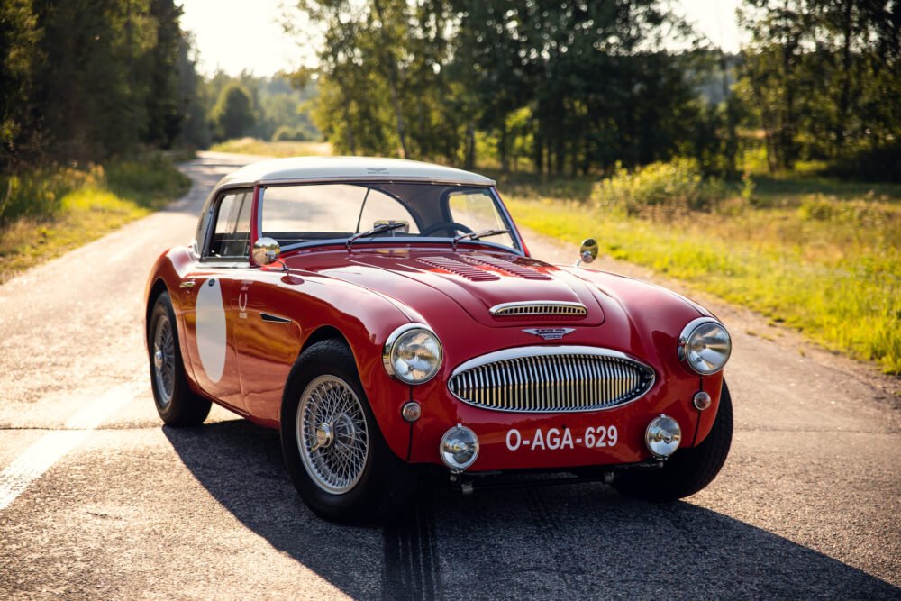 Vintage red sports car on sunny forest road.