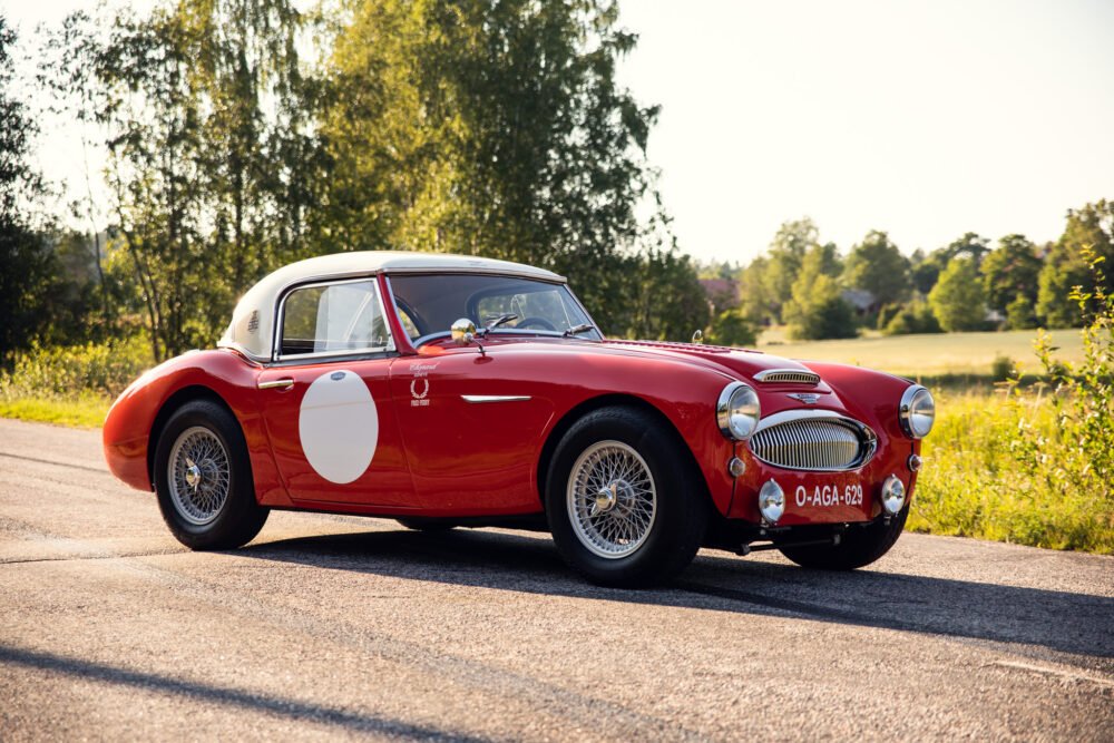 Vintage red sports car on rural road at sunset.