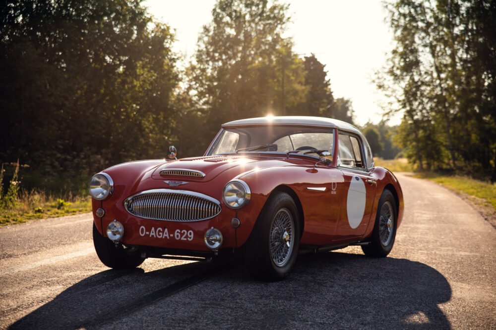 Vintage red sports car on sunny forest road.