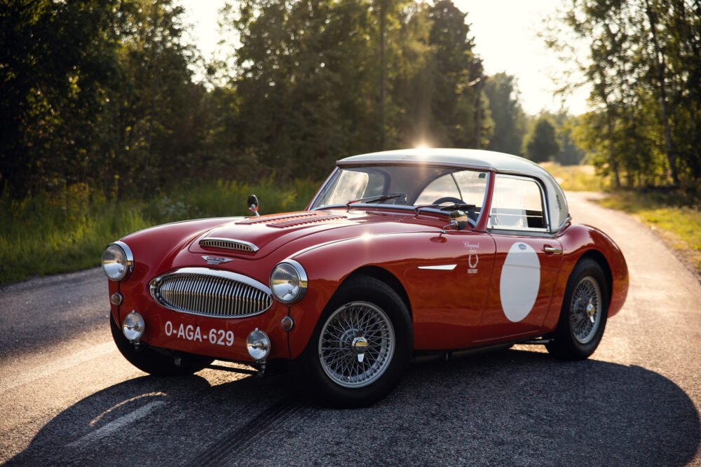 Vintage red sports car on forest-side road at sunset.