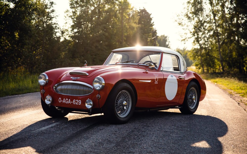 Vintage red sports car on forest road at sunset.