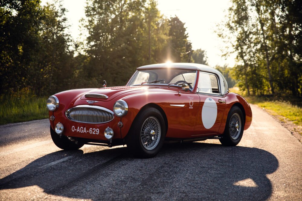 Vintage red sports car on forest road at sunset.