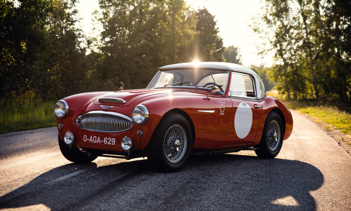 Vintage red sports car on forest road at sunset.