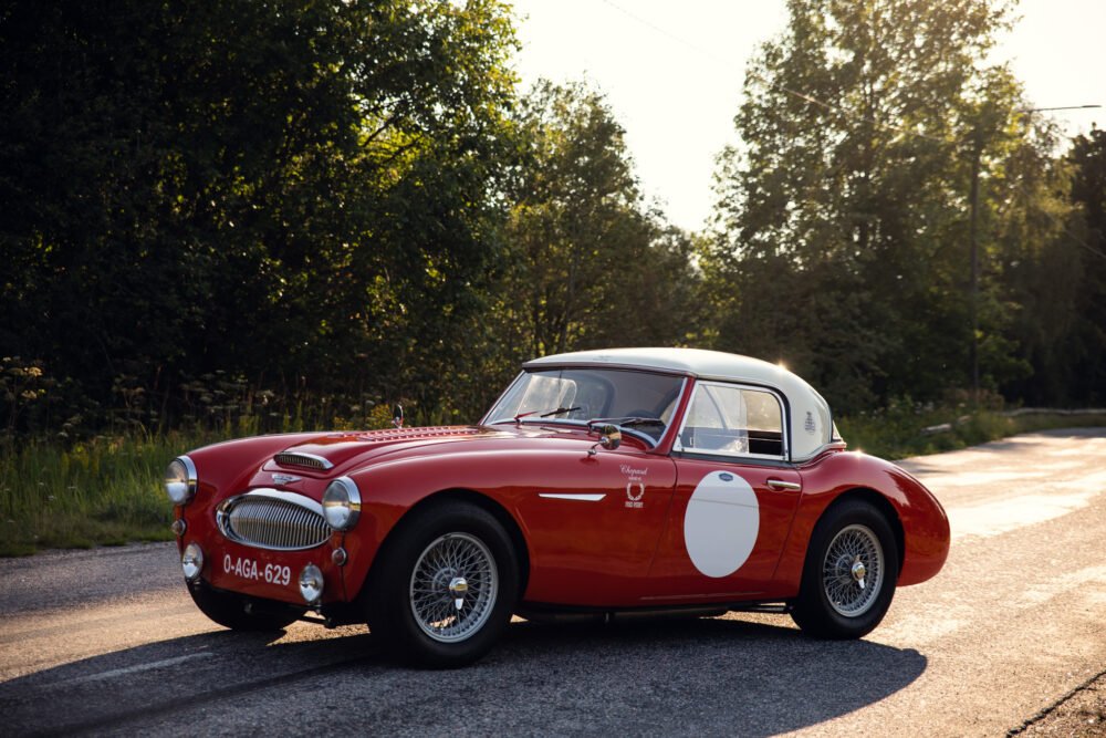 Vintage red sports car on forest-lined road.