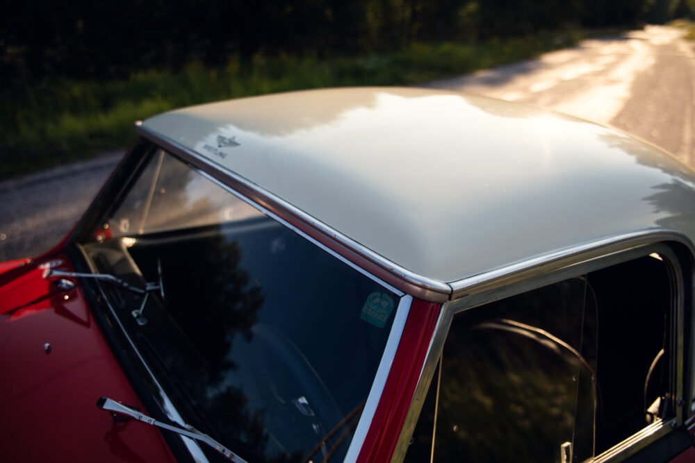 Vintage red car's roof with Mustang emblem on road.