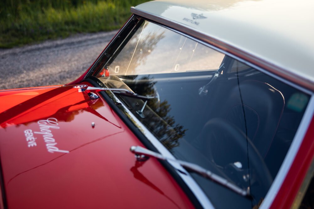 Close-up of vintage red car's elegant windshield and logo.