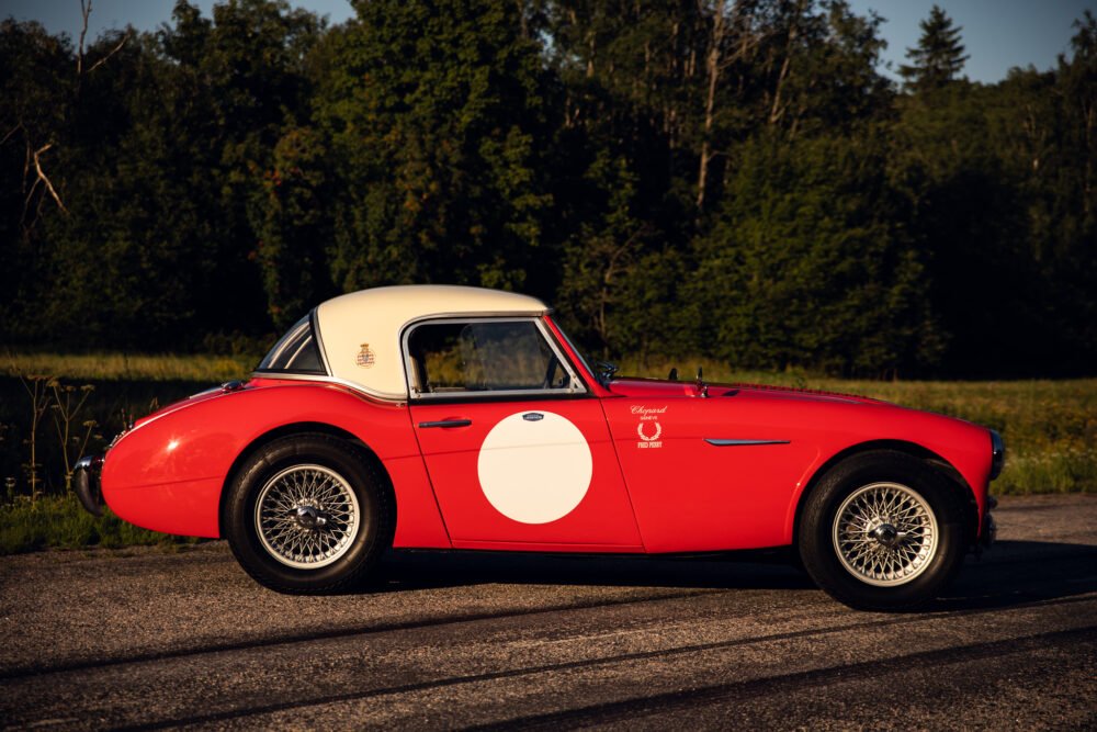 Vintage red sports car on forest-lined road.