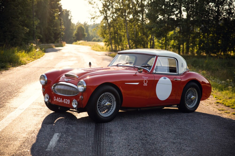 Vintage red sports car parked on sunny forest road.