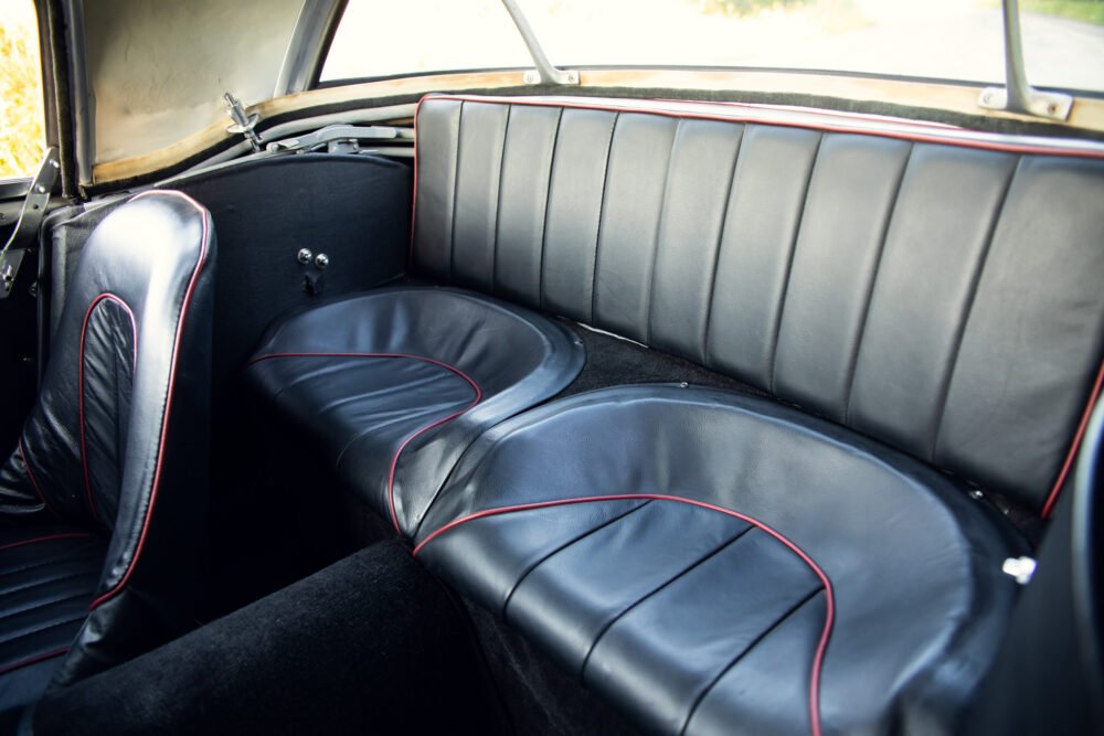 Vintage car's black leather backseat with red trim.