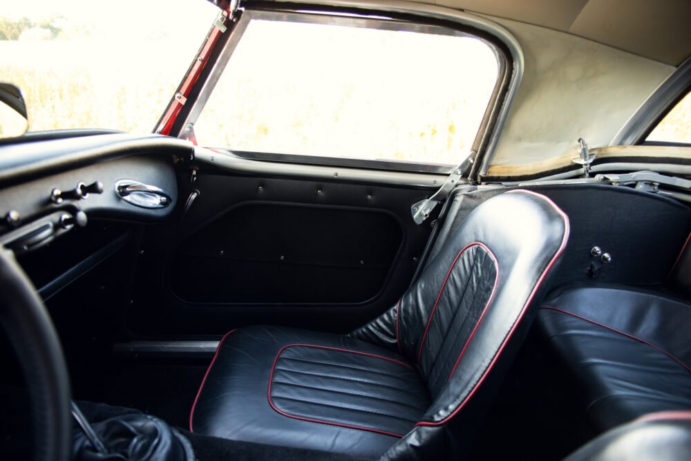 Vintage car interior with red stitching and open roof.