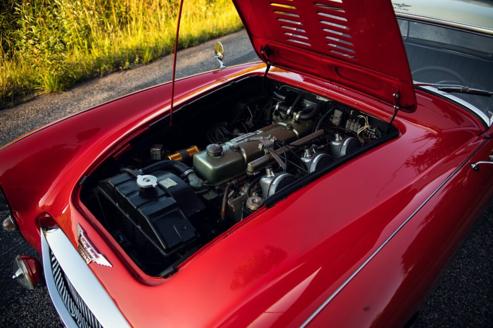 Red vintage car engine open on road.