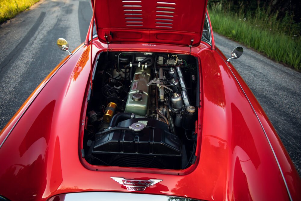 Red vintage car engine bay open on road.